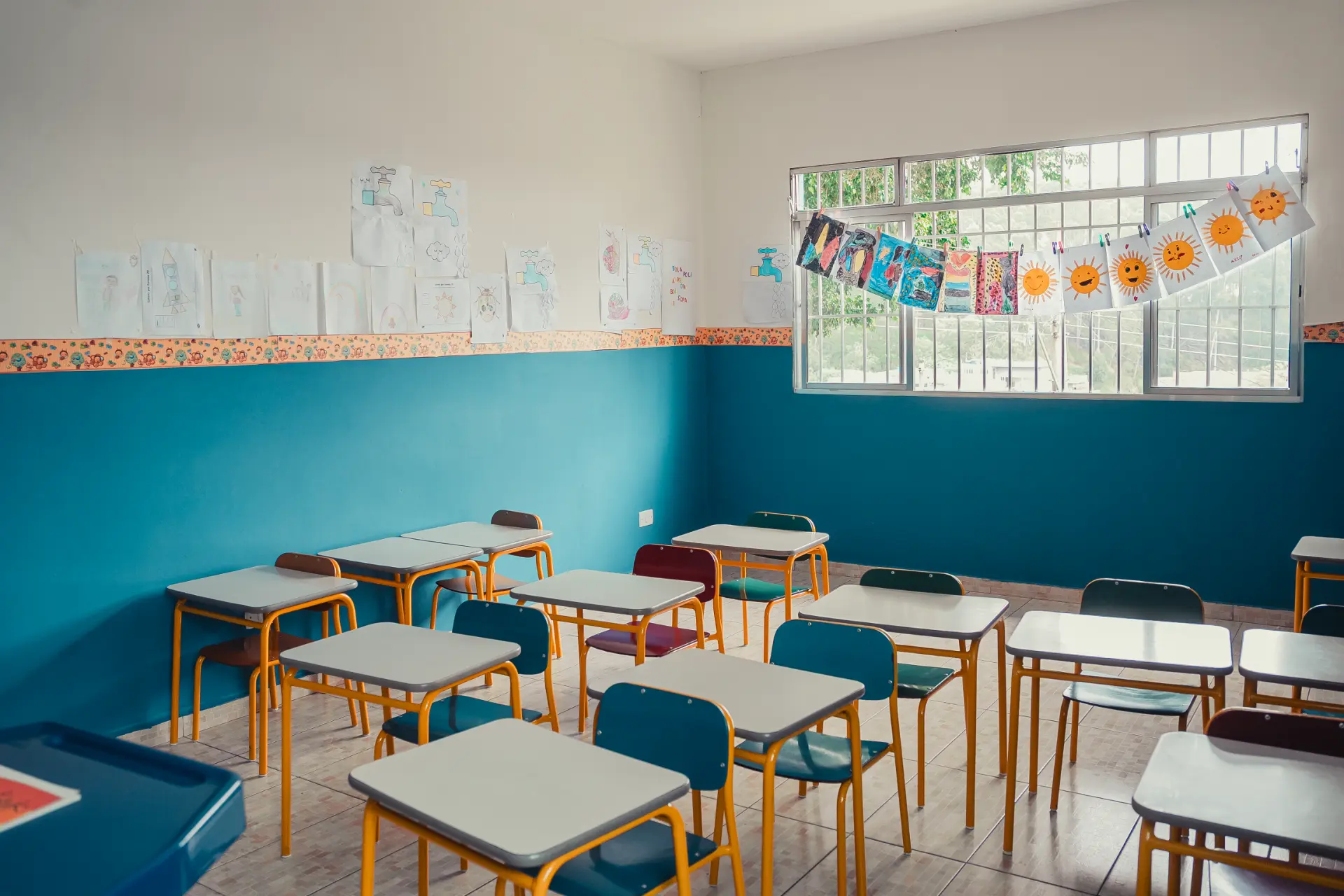 Sala de aula com carteiras amarelas organizadas e desenhos das crianças na parede